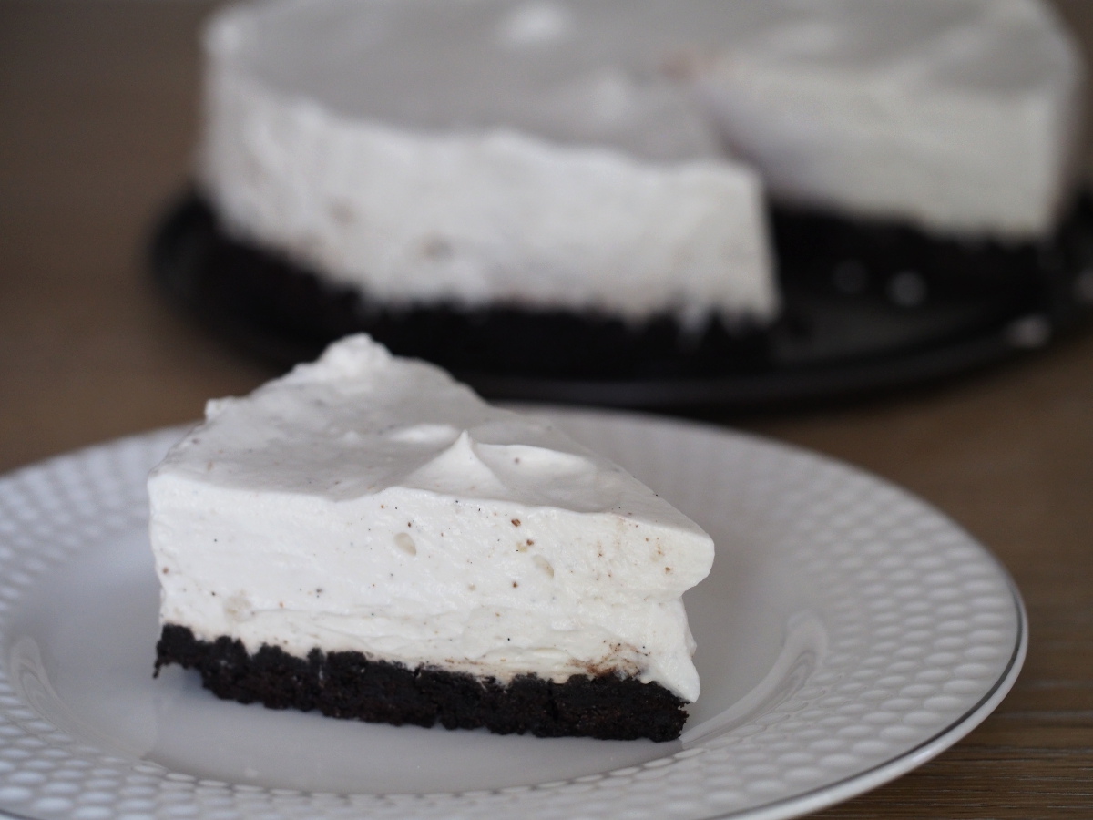 Ein Stück der Oreo-Torte auf einem Kuchenteller im Vordergrund, im Hintergrund der Rest der kleinen Torte.