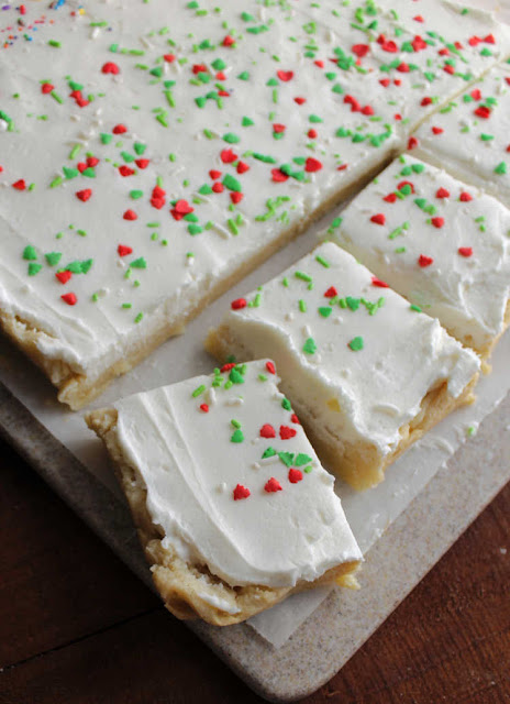 Super soft sugar cookie bars topped with a fluffy layer buttercream are a fun and easy treat. They are so much quicker to make than individual cookies and taste great! pieces of sugar cookie bar cut in squares with white buttercream and sprinkles on top
