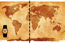 Pequena imagem retangular de um mapa mundi. O fundo, que representa o oceano está em cor bege amarelada, os continentes estão em cor marrom, de diferentes nuances de tonalidade. No canto esquerto abaixo, se vê um desenho simples de relógio de pulso, na cor preta. Também, na cor preta linha grossa pontilhada vetical, representando no mapa o Meridiano de Greenwich, que divide o Mundo em Ocidente e Oriente.