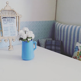 Detail of a a menu and jug of daisies on a table in a one-twelfth scale modern miniature cafe scene.