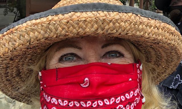 A close-up photo of a woman wearing a straw hat and a red face mask