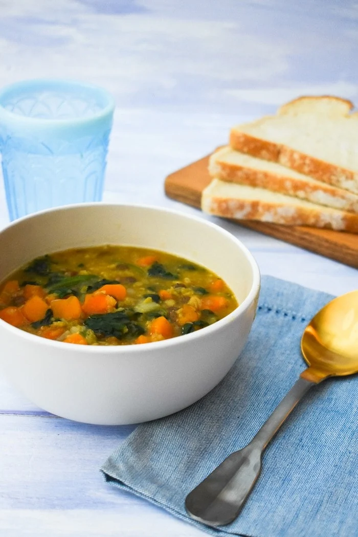 Sweet Potato, Green Lentil & Spinach Soup in a cream bowl with pale blue napkin and gold spoon