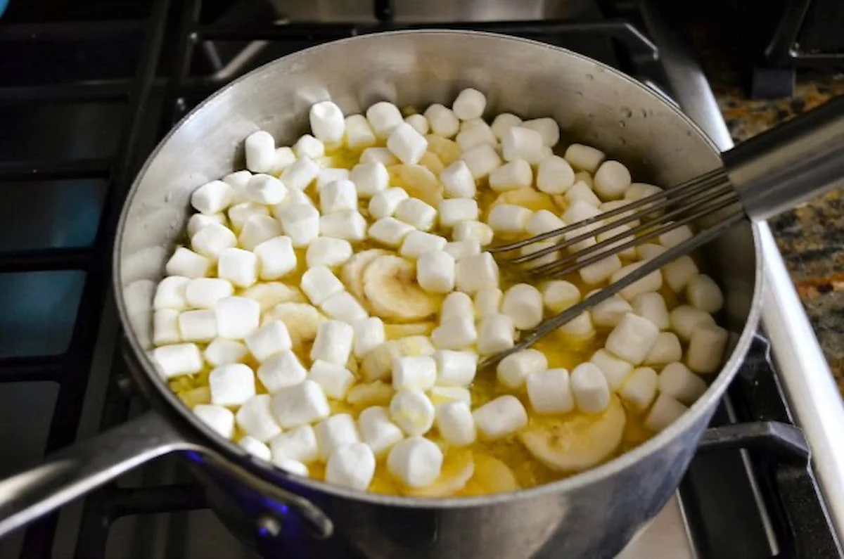 7 Up Jello with Marshmallows, Bananas, and Crushed Pineapple being stirred into a saucepan.
