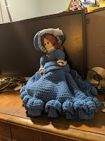 The Other Suitcase Doll stands tall in blue crocheted dress and hat, somewhere between schoolmarm and dance hall girl