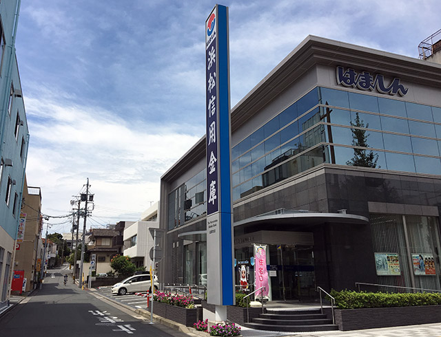 浜松城大手前の諏訪神社大祝家邸宅跡地に建つ浜松信用金庫伝馬町支店と諏訪神社参道、遠く坂上にははまホールが見える(2017年8月23日撮影)
