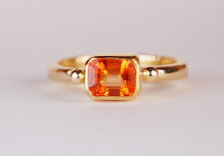 Simple ring with an emerald cut orange sapphire in a bezel setting