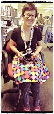 Little Colourful Teacher with Kwokkie Doll on her lap. They are both dresed in the same outfit of a black top with a polka-dotted skirt.