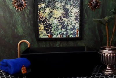 One-twelfth scale modern miniature bathroom with green marbled wall, black bath and a gold tap. Outside the window above the bath is a vertical garden.