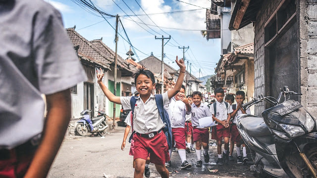 gambar murid SD sedang mengangkat tangan dan tertawa bersama teman-temannya di indonesia dengan baju putih dan celana merah