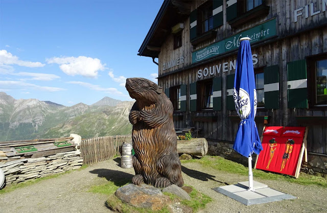 Murmeltier Figur aus Holz vor Holzhaus am Fuscher Lake, Berge, Sonne