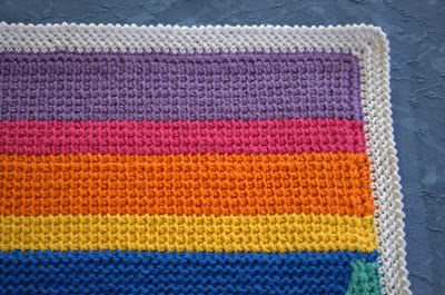 Tricot placemat in a rainbow of coloured stripes with a white herringbone stitch border.