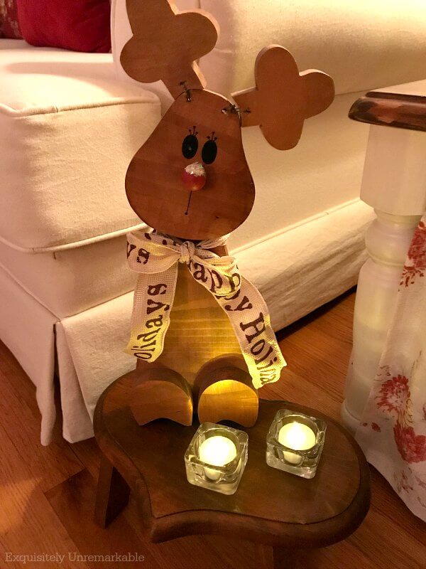 Wooden reindeer statue seated on a heart stool with votives around it