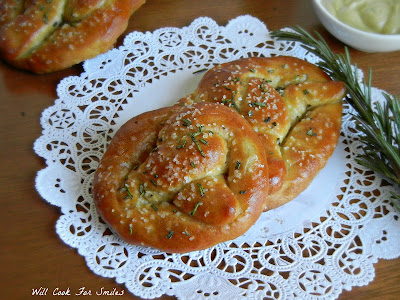rosemary soft pretzels on a lace napkin with a sprig of rosemary to the right 