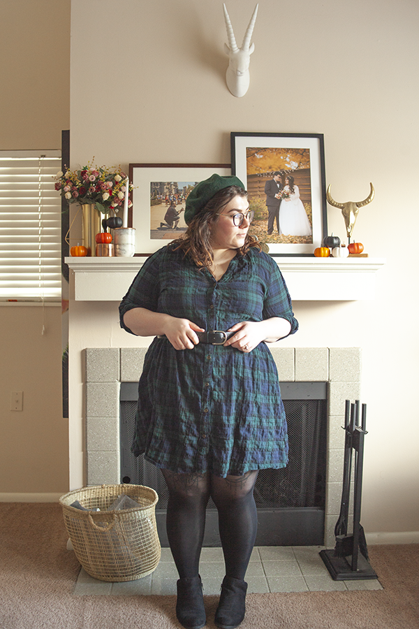 An outfit consisting of a green beret, green and blue plaid smock baby doll dress, black tights and black ankle boots.