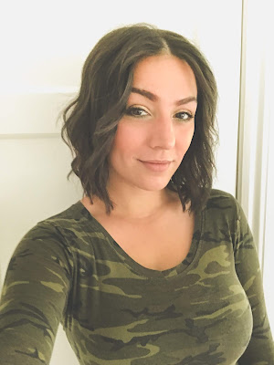 A picture of me with short curled hair just above my shoulders. I am wearing a camo bodysuit. This is after my haircut.