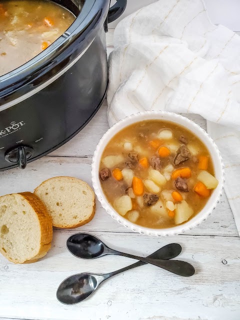 Easy Slow Cooker Beef Stew in a white bowl sitting next to a slow cooker.
