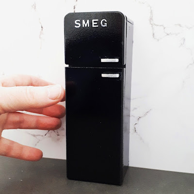 One-twelfth scale modern miniature retro Smeg fridge with a had next to it for scale.