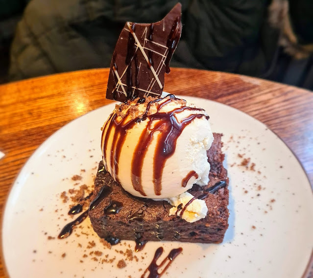 Image of a gluten free dessert consisting of chocolate brownie, topped with vanilla ice cream, drizzled in chocolate sauce and topped with a chocolate shard.
