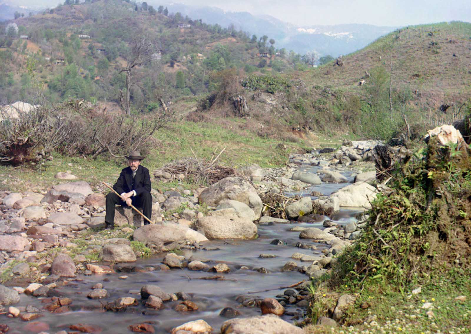 Self-portrait on the Karolitskhali River, ca. 1910. Prokudin-Gorskii in suit and hat, seated on rock beside the Karolitskhali River, in the Caucasus Mountains near the seaport of Batumi on the eastern coast of the Black Sea.