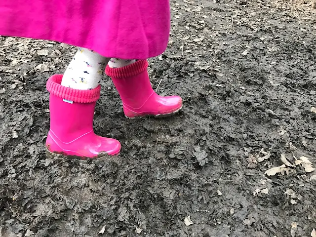 A girl wearing a pair of pink Term wellies and walking in wet mud mixed with dried leaves