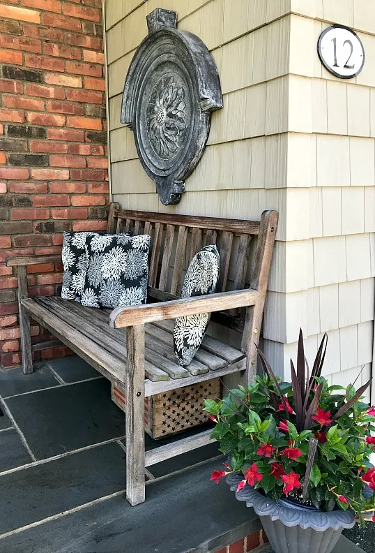 Teak bench at front of house with potted plant in iron planter