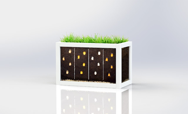The image shows a clear planter box with white wooden outlines. The box has glass panels so you can see the soil inside. Inside the soil is compostable coffee pods and there is grass growing on the top.