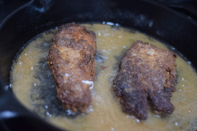 The breaded chicken cooking in the frying pan. 