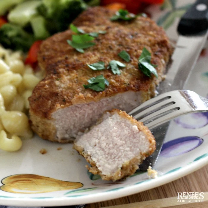 Piece of cut breaded oven baked pork chop on fork with rest of pork chop on plate