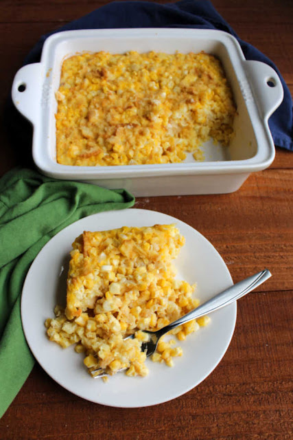 Scalloped corn is a vintage comfort food side dish recipe that deserves a spot on your plate. Twists on this recipe happen to be in the recipe boxes of great grandmas on both sides of my family and both families loved it when they would whip some up. Serve scalloped corn for a simple, filling and delicious way to round out your dinner plate. Your family will be glad you did! serving of old fashioned scalloped corn on plate with casserole in background