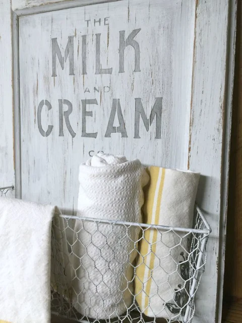 White cabinet door with milk and cream stencil and white basket with towels