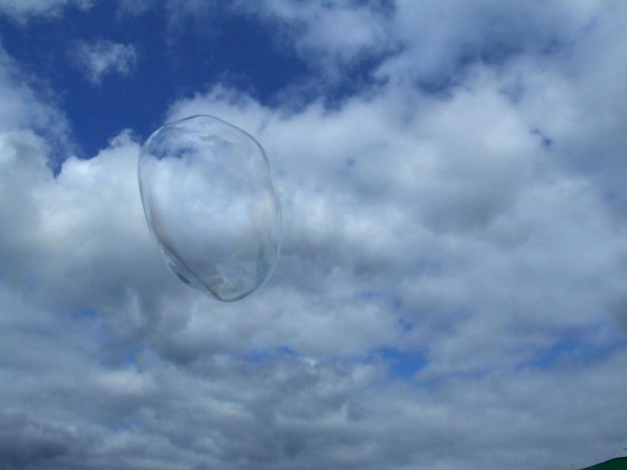 真っ青な空と白い雲に、シャボン玉が飛んでいる風景の写真素材です。どこかファンタジックで非日常な印象を与えます。