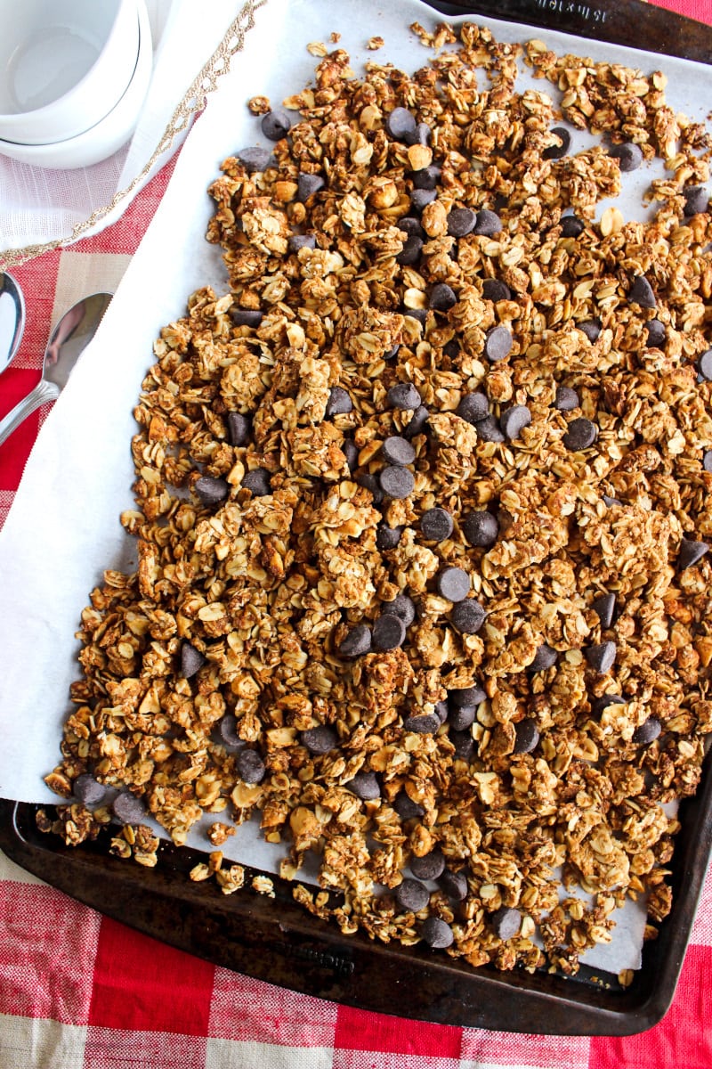 Chocolate Chip Peanut Butter Granola | The Two Bite Club Chocolate Chip Peanut Butter Granola on a parchment-lined baking sheet on a red and white checkered background.