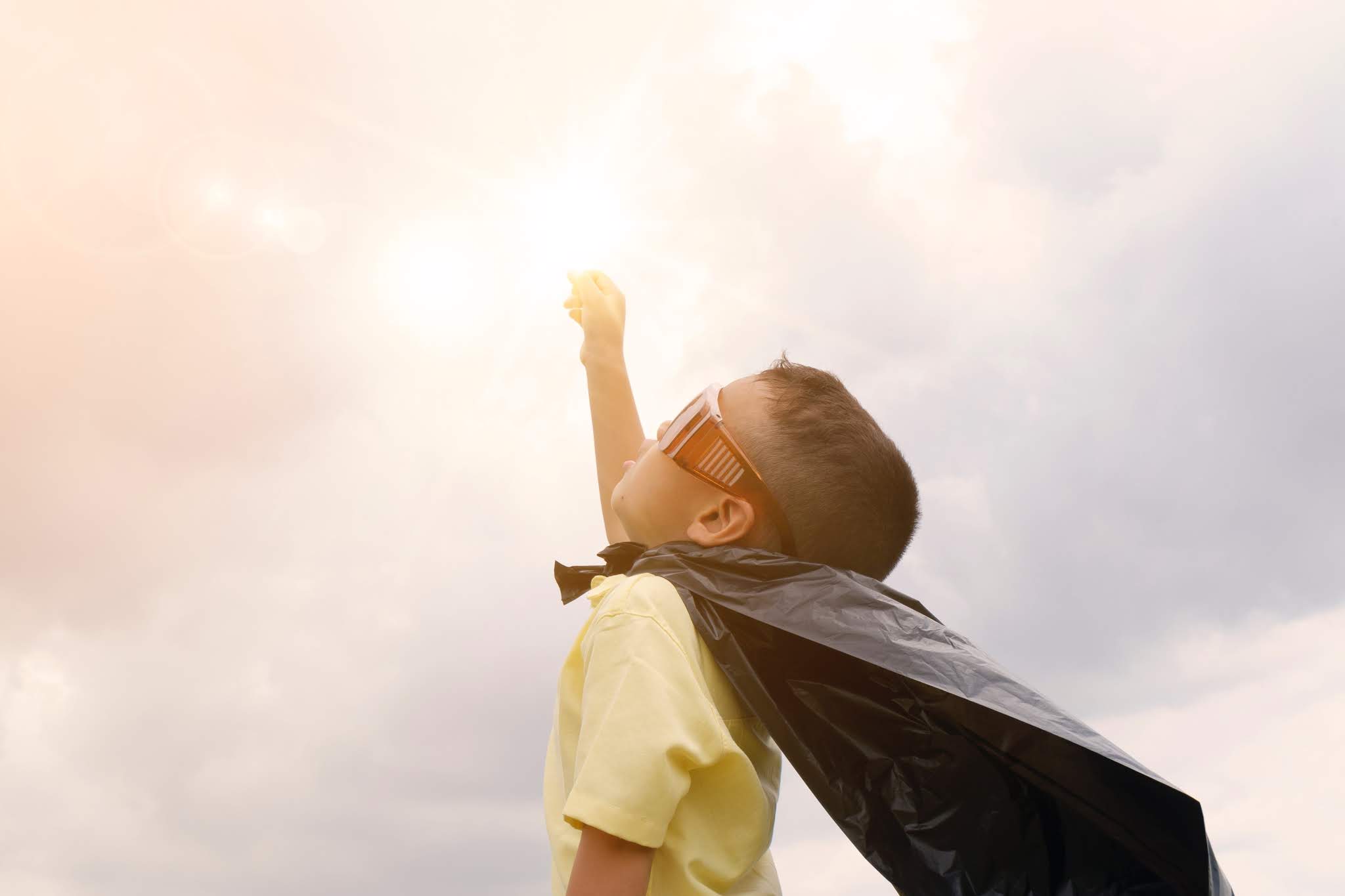 kid dressed as super hero pointing fist towards sky