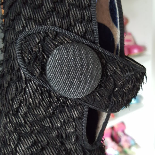 close up of decorative button on thick strap of shoe with shoe shelves in background