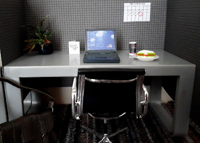 One twelfth scale modern miniature office cubicle with a laptop, a sandwich and takeaway coffee, a thank you card and a December 2020 calendar with 11 December circled with a red smiley face.