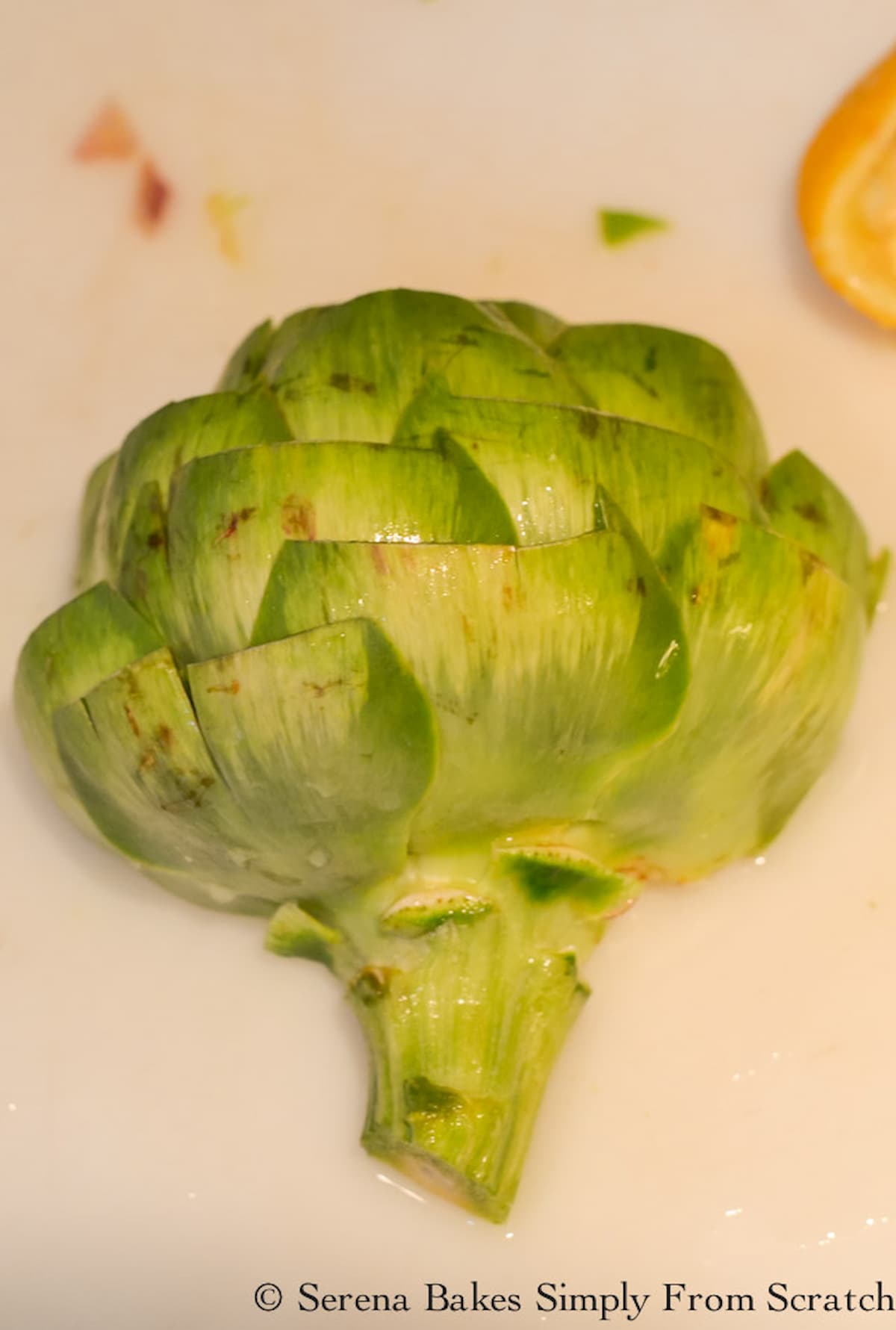 An Artichoke cut in half laying cut side down on a cutting board with lower leaves removed.