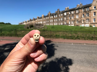 Skulferatu #40 - a photo of a Skulferatu, small ceramic skull, behind help with Muschet's Cairn on Duke's walk, Holyrood Park in the background.  Photo by Kevin Nosferatu for the Skulferatu Project