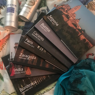 Two bottles of bubble bath, next to a stack of books with titles like Segovia September 2012 and India February 2018. In the bottom-right corner is some teal-coloured tulle with tigers embroidered on it.