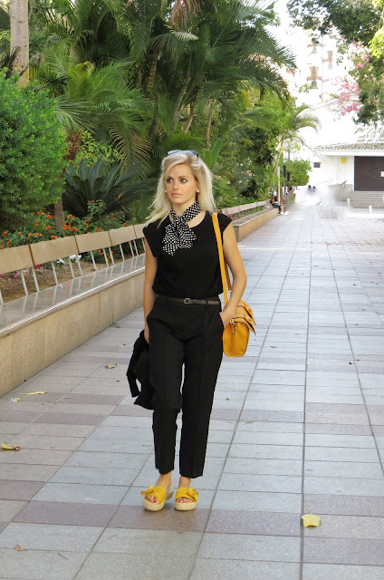 Alejandra Colomera con camiseta negra, pantalón formal negro, lazo en el cuello negro con lunares blancos y complementos mostaza