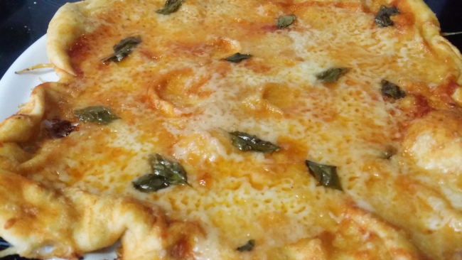 una pizza con queso, tomate y albahaca