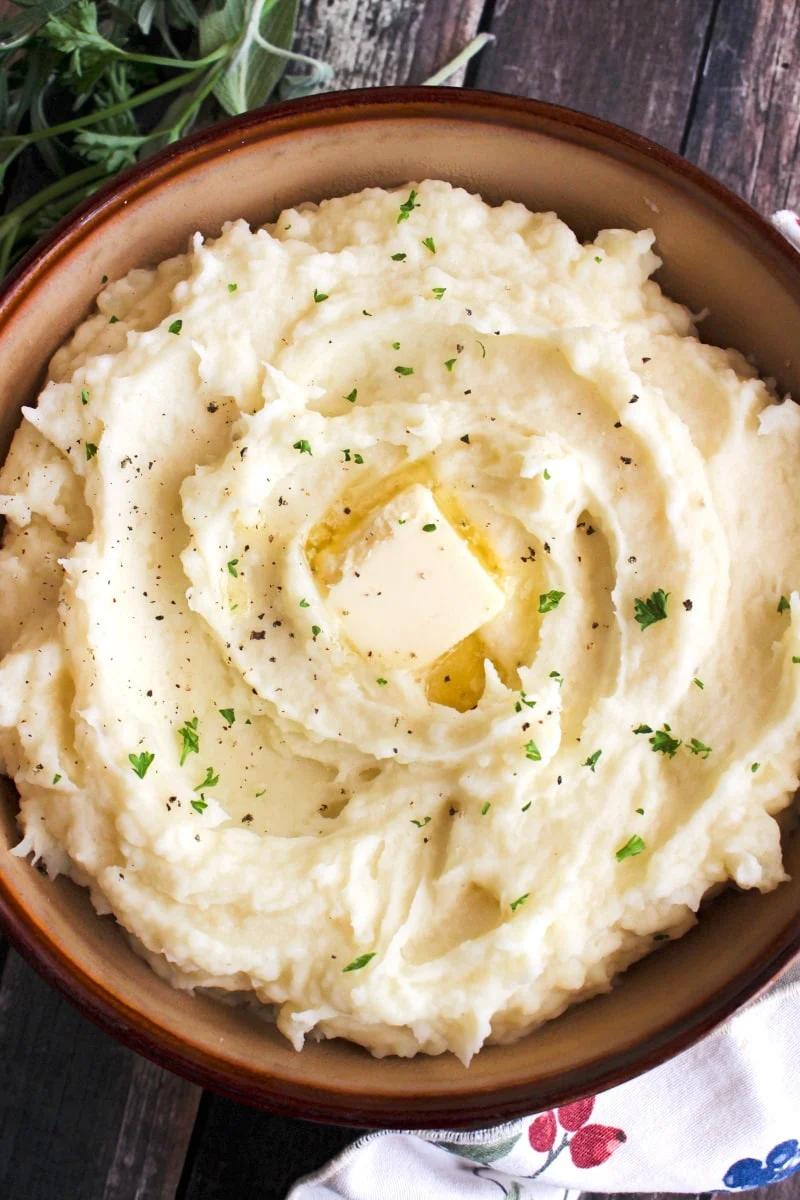 Top view of Instant Pot Mashed Potatoes in a brown bowl on a rustic wood background.