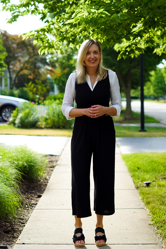 A woman stands on a sidewalk and demonstrates How to Wear a Sleeveless Jumpsuit to Work