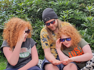 3 boys 12 to 22 sitting on grass all examining things wearing EnChroma glasses