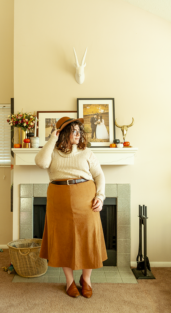 An outfit consisting of a brown panama hat, a cream cowl neck sweater half tucked into a brown A-line tea length skirt and a cognac d'orsay flats.
