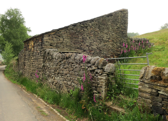Old farm building, dry stone wall, metal gate and grassy field.