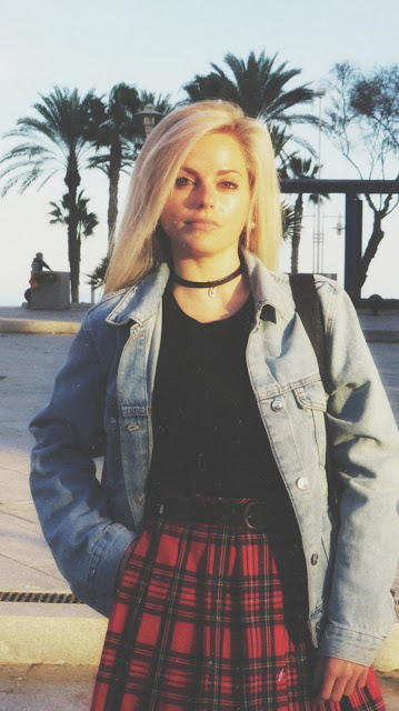 Estilo grunge con camiseta negra, falda de tablas tartán, medias de red grande, botas estilo militar y cazadora vaquera