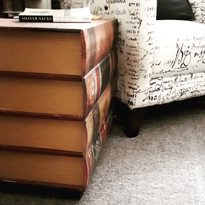 Side table made to look like a stack of giant books, next to an armchair.