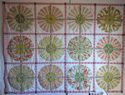 Center of the wheel quilt sewn Wheel composed of four fan blocks with alternating pale red and green blades sashed with tan are in turn sashed with red and white stripe in this low volume quilt