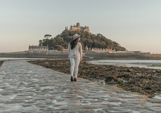 a girl stands on the cobbled pathway, with a view of St Michael's Mount ahead of her.