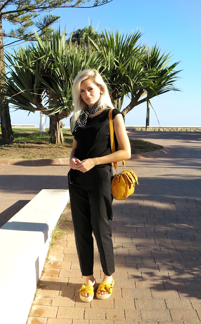 Alejandra Colomera con camiseta negra, pantalón formal negro, lazo en el cuello negro con lunares blancos y complementos mostaza